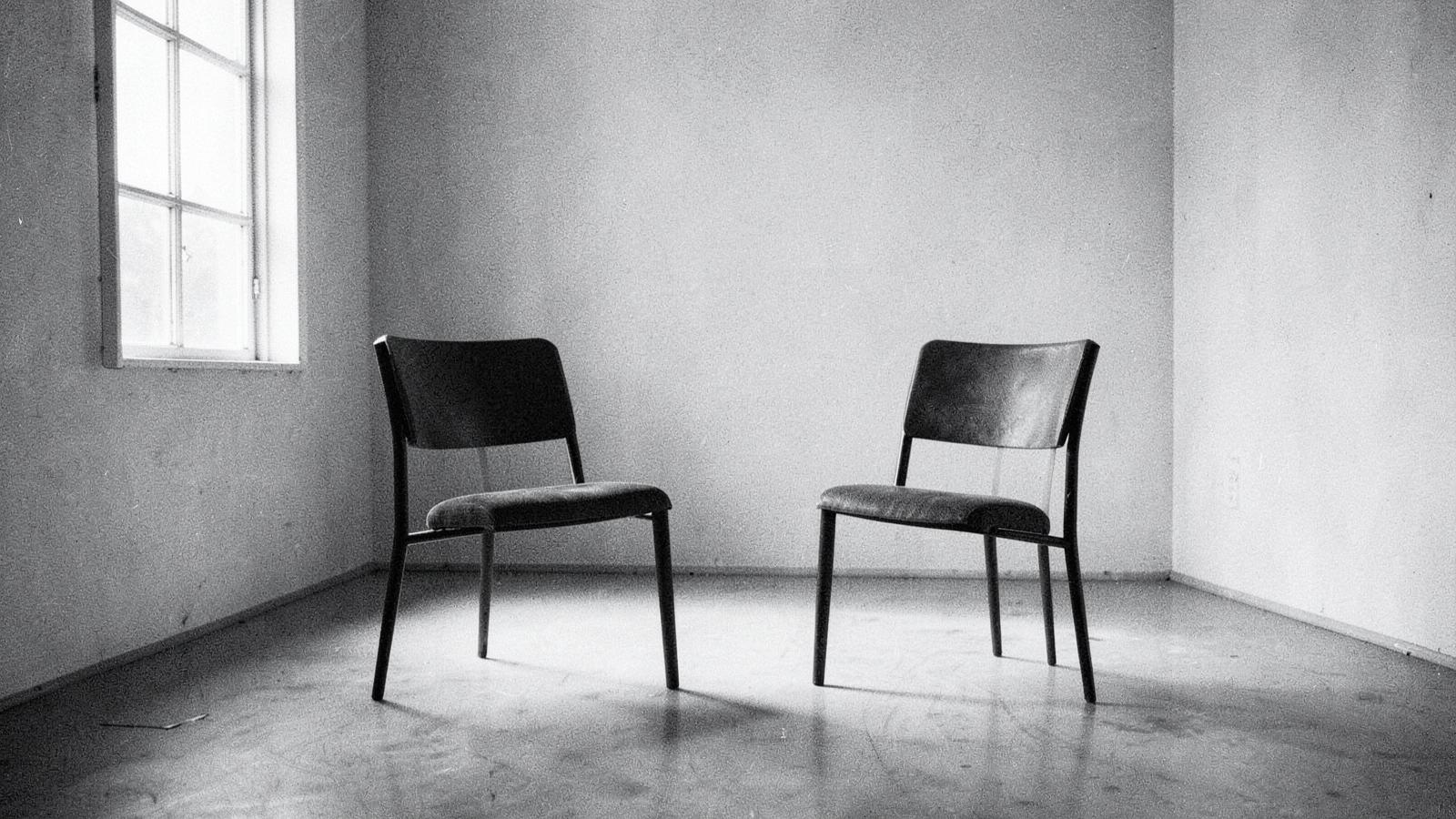 Two empty chairs facing each other in a bare, sunlit room